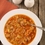 An overhead view of Instant Pot cabbage, ground turkey and smoked sausage soup in a bowl with a spoon on a rustic wooden surface.