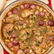 A cast iron pan filled with boneless chicken thighs braised in red wine with bacon, thyme, mushrooms, and pearl onions.