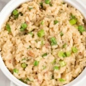 A round, white serving bowl filled with creamy risotto with sautéed pancetta, peas, and scallions.