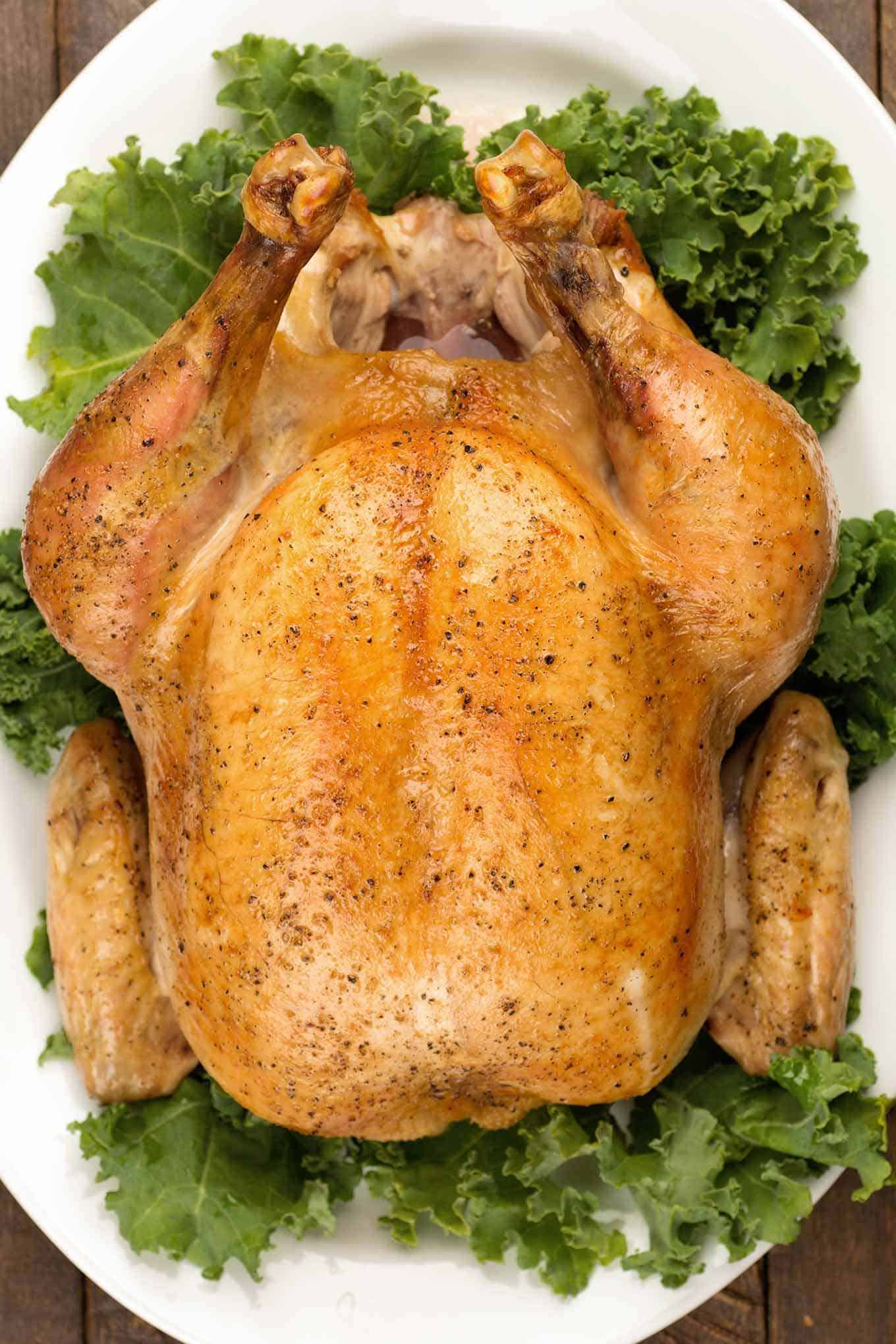 Perfectly-browned roastrf capon on a serving platter garnished with raw kale.