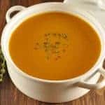 White ceramic bowl filled with smooth roasted butternut squash and chestnut soup, garnished with fresh thyme on top.