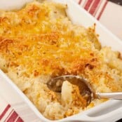 Golden brown roasted cauliflower gratin topped with melted cheddar cheese and crispy breadcrumbs in a white baking dish with serving spoon.