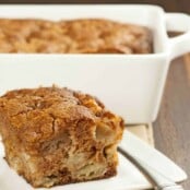 A single serving of spiced apple pudding cake on a plate with the whole cake in the background.