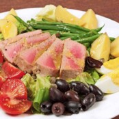 Classic Salad Niçoise with seared tuna slices, hard-boiled eggs, cherry tomatoes, olives, green beans, capers, and potatoes on a bed of fresh lettuce.