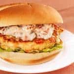 A grilled salmon burger topped with sun-dried tomato and chive mayonnaise on a lettuce-lined bun, served on a white plate.