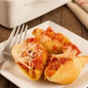 Sausage stuffed pasta shells topped with marinara and melted cheese, served on a white plate with a fork.