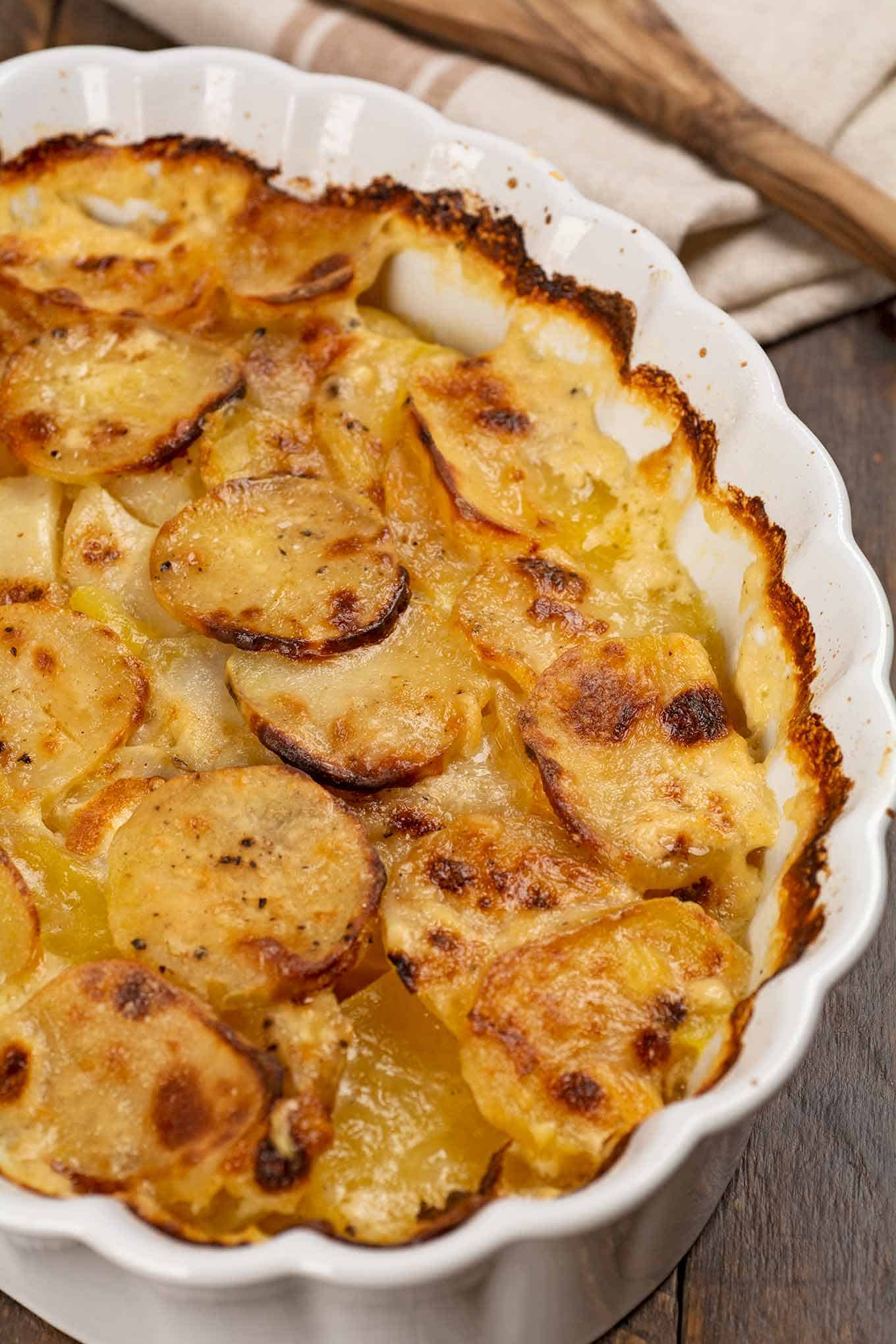 An oval, white baking dish of scalloped potatoes with a serving removed in order to see the layers.
