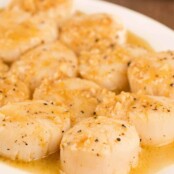 Seared scallops drizzled with lemon and garlic pan sauce, served on a white plate, sprinkled with black pepper.