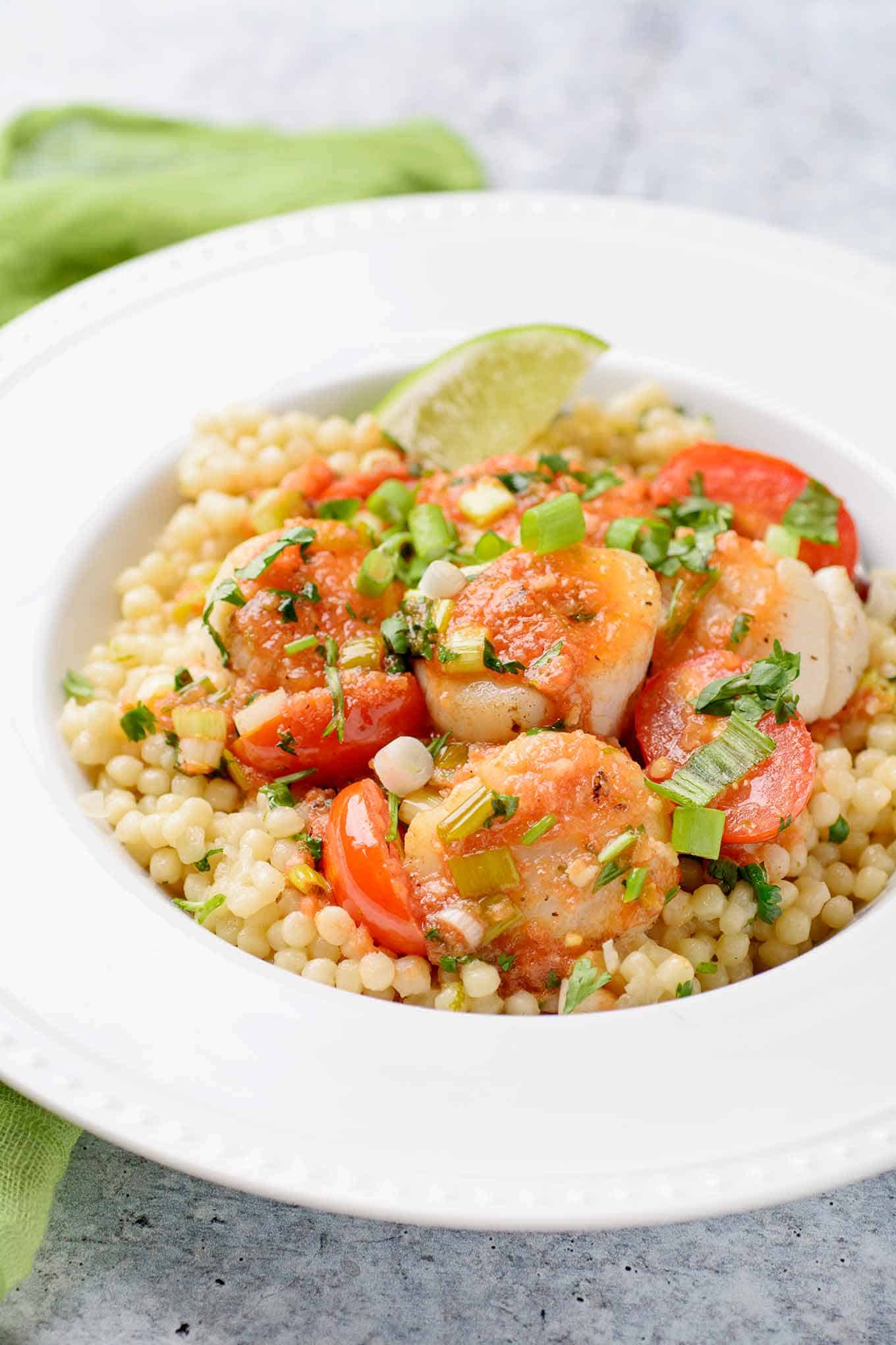 Scallops in tomato-lime butter garnished with chopped cilantro and a lime wedge.