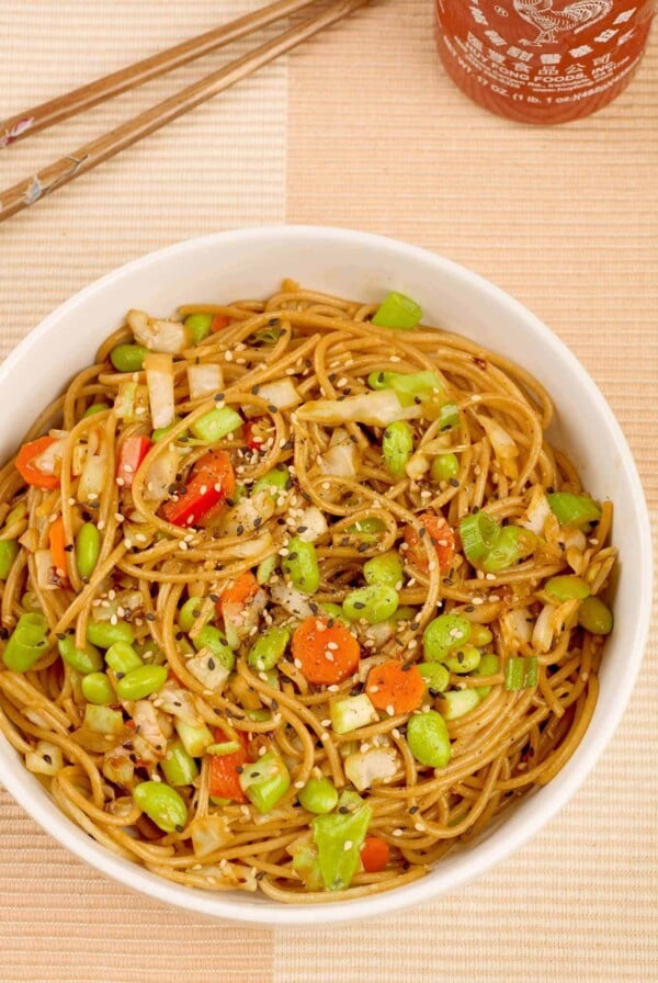 A bowl of whole wheat spaghetti tossed with edamame, stir-fried cabbage, sesame seeds and a light peanut sauce.