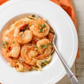 A shallow pasta bowl filled with a serving of Shrimp Fra Diavolo (Italian-style shrimp in spicy tomato sauce) with a fork in the bowl, napkin underneath.