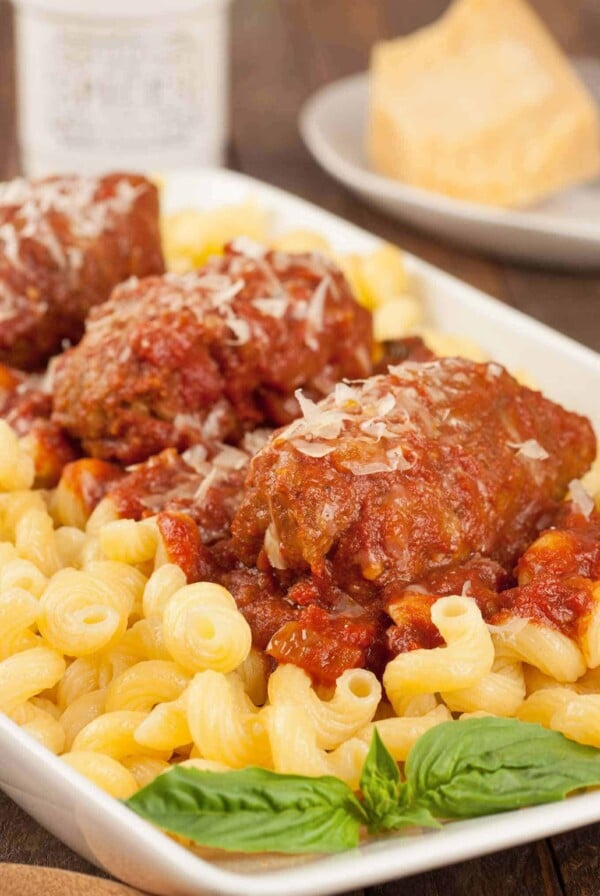 Slow cooker beef braciole topped with tomato sauce and Parmesan, served over cavatappi pasta with fresh basil garnish.