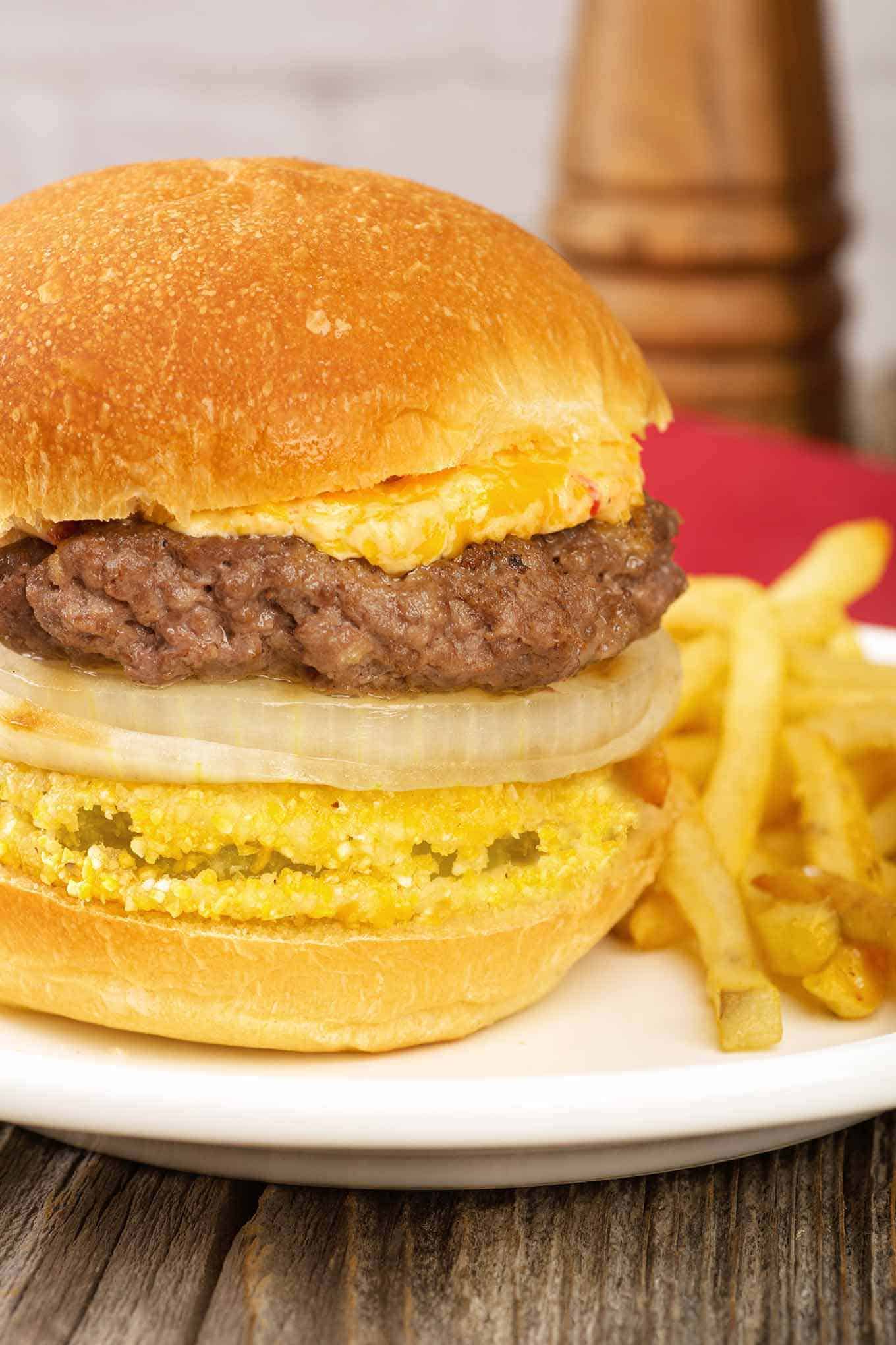 Bun stacked with fried green tomato, grilled onion, beef burger, and creamy pimento cheese.