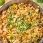 A frying pan filled with Southwest-style chicken and cauliflower rice with bell peppers, corn, scallions, beans, garnished with sliced jalapenos and cilantro.