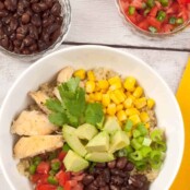 An overhead view of Southwest chicken quinoa bowl with black beans, corn, avocado, diced tomatoes, green onions, and fresh cilantro.