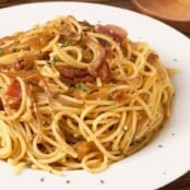 A plate of spaghetti tossed with crispy bacon, caramelized onions, and fresh thyme on a white dish.
