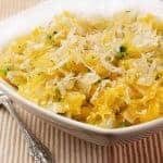 Spaghetti squash mixed with sautéed onion, garlic, and herbs, topped with grated cheese in a white bowl.