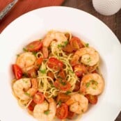An overhead view of a serving of thin spaghetti tossed with chunks of chorizo, sautéed garlic and onion, jumbo shrimp simmered in sherry, and grape tomatoes.