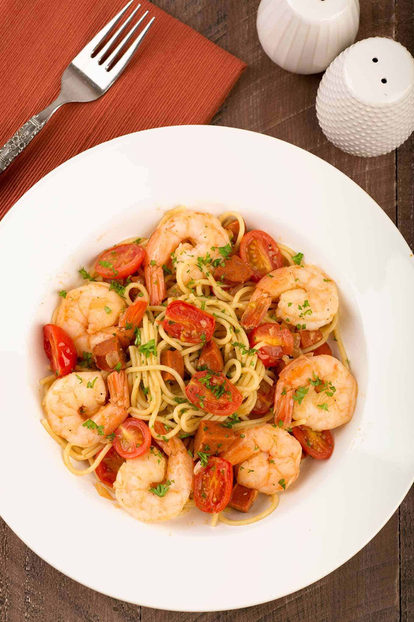 Single serving bowl of spaghetti with shrimp, chorizo, fresh tomatoes and parsley garnish.