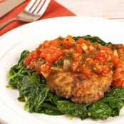 A plate of lightly breaded steak alla Milanese topped with tomato sauce, served over a bed of sautéed spinach.