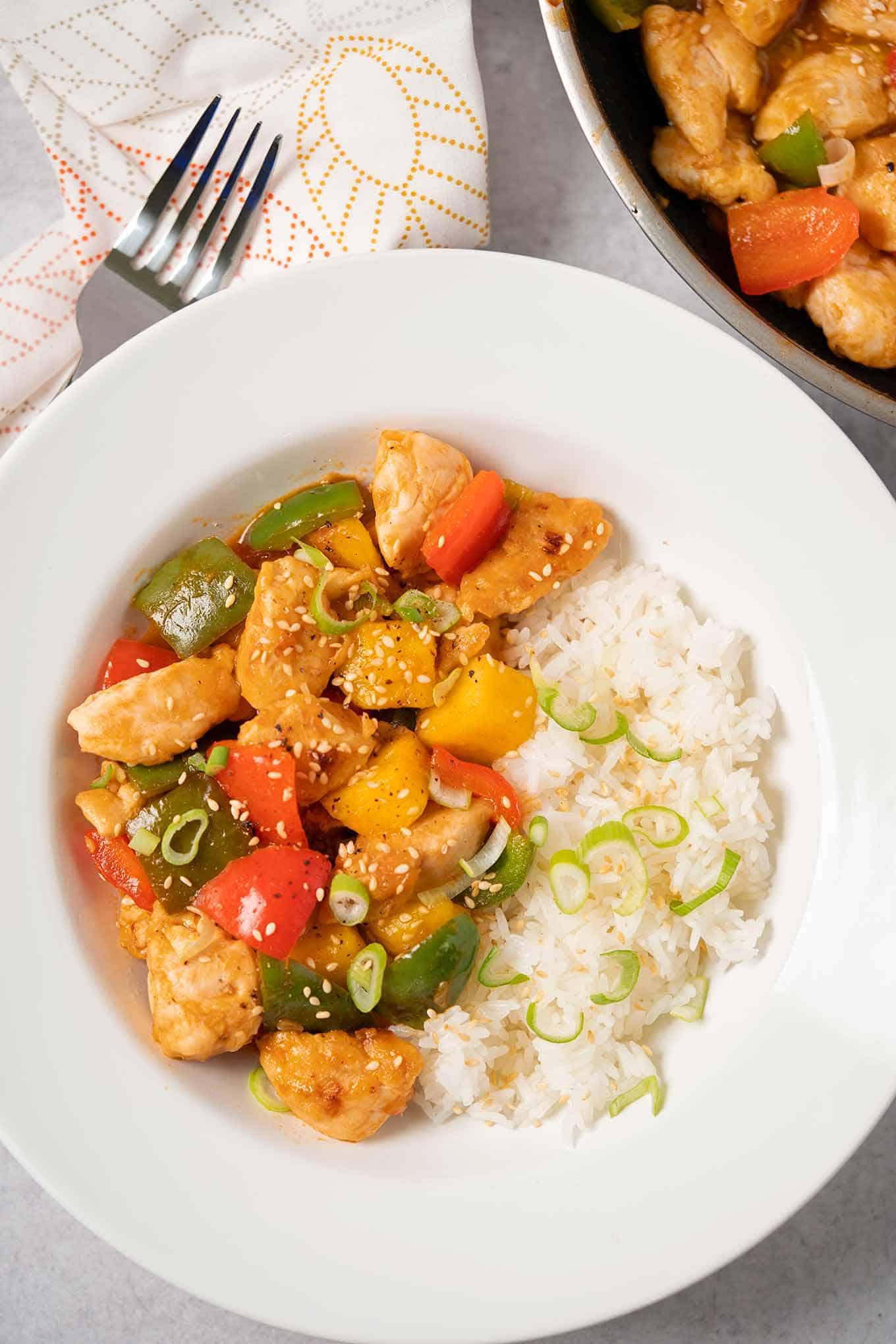 Sweet and sour chicken with pineapple in a bowl garnished with sesame seeds and scallions.
