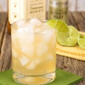 A rocks glass filled with a cocktail of Jack Daniel's Tennessee Honey Whiskey combined with ginger beer and garnished with lime, bottles and sliced lime in the background.