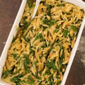An overhead view of a casserole of toasted orzo and sautéed spinach side dish, with a serving spoon.