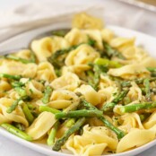A serving plate filled with delicate cheese tortellini tossed with roasted asparagus, lemon zest, parsley, and a light cream sauce.