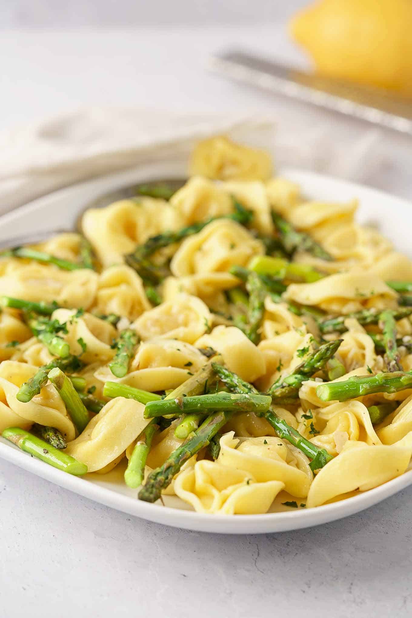 A serving plate filled with delicate cheese tortellini tossed with roasted asparagus, lemon zest, parsley, and a light cream sauce.