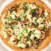 Top view of an uncut pizza topped with spinach, mushrooms, goat cheese, and mozzarella.