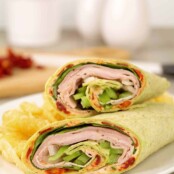 A sandwich wrap filled with sliced turkey, ham, green pepper, provolone cheese, and a sun-dried tomato spread.