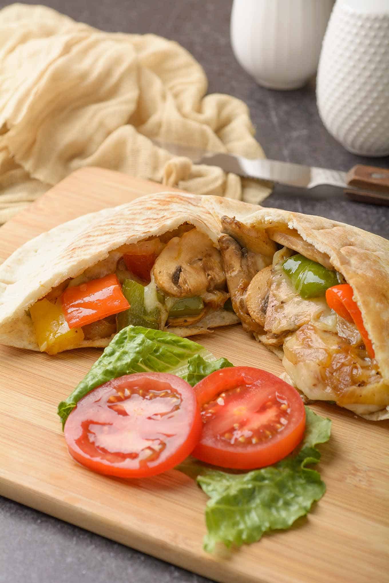 Pepper and mushroom pita sandwich on cutting board with fresh lettuce and tomato