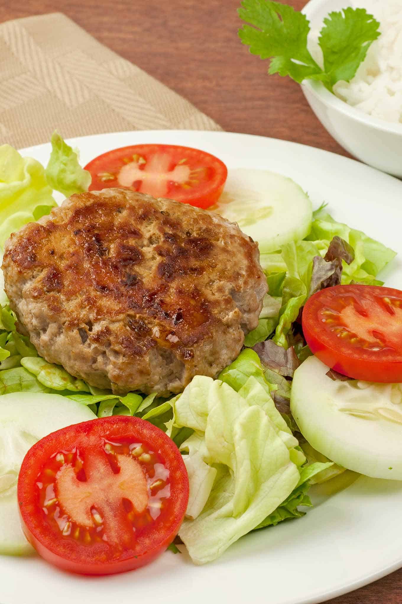 Vietnamese pork patty on a bed of lettuce surrounded by sliced cucumber and tomatoes.