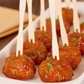Whiskey glazed cocktail meatballs served in a white dish with wooden cocktail picks, garnished with chopped parsley.